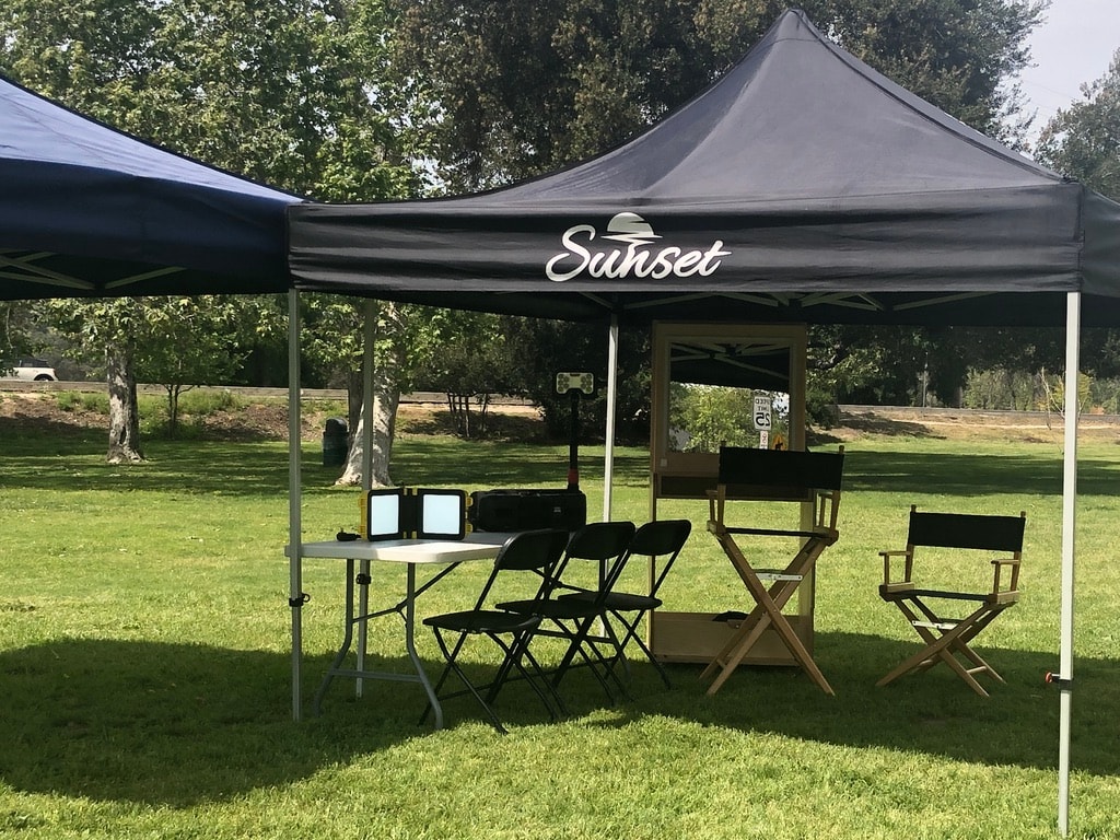 Black Sunset tent with director's chairs and a makeup mirror in a park