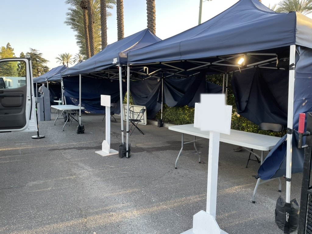 Row of navy Sunset tents with sidewalls and check-in tables in a parking lot