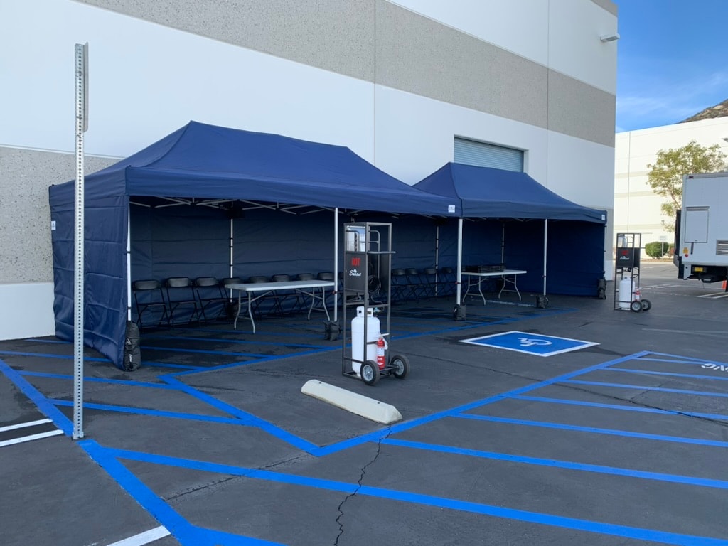 Navy Sunset tents with sidewalls, tables, chairs and propane heaters in a parking lot
