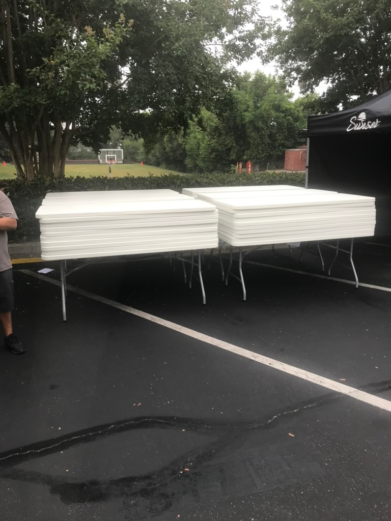 Stacks of white banquet tables ready for delivery beside a black Sunset tent